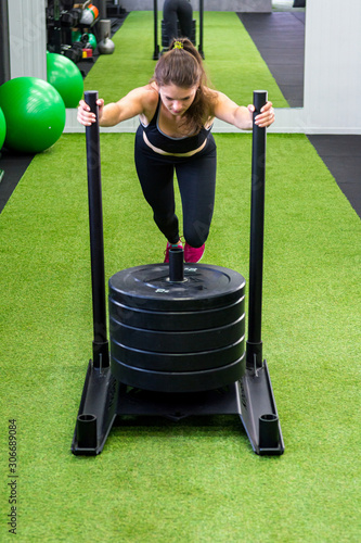 Young female fitness trainer performing sled push in local gym.