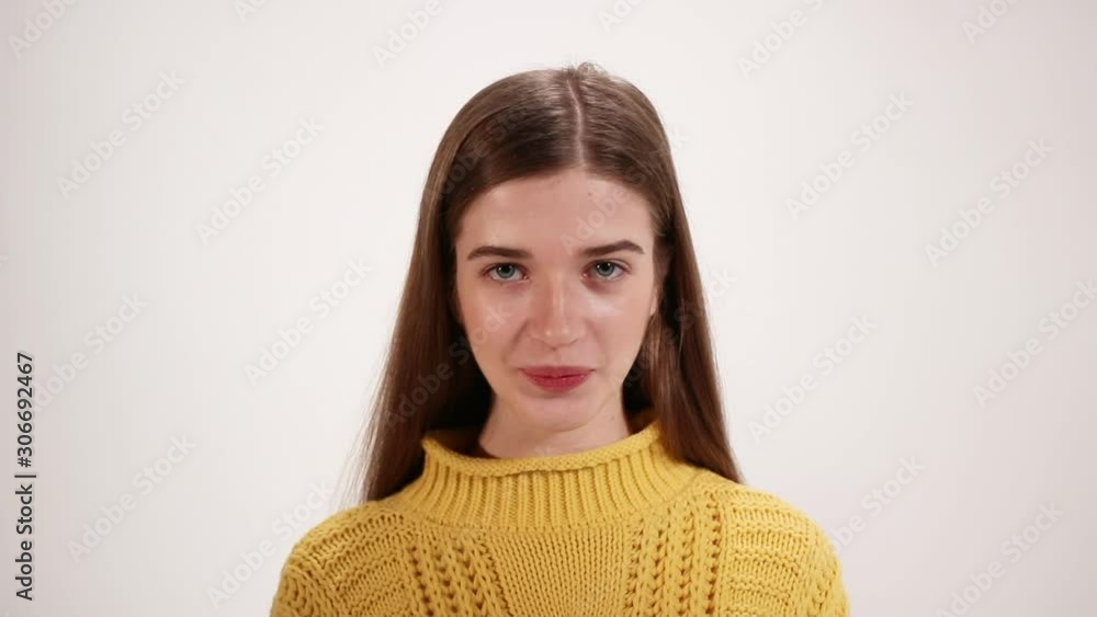 Close up view of smiling girl in yellow sweater showing silence gesture and looking at the camera over white background Close up view of smiling girl in yellow sweater showing silence gesture and looking at the camera over white background