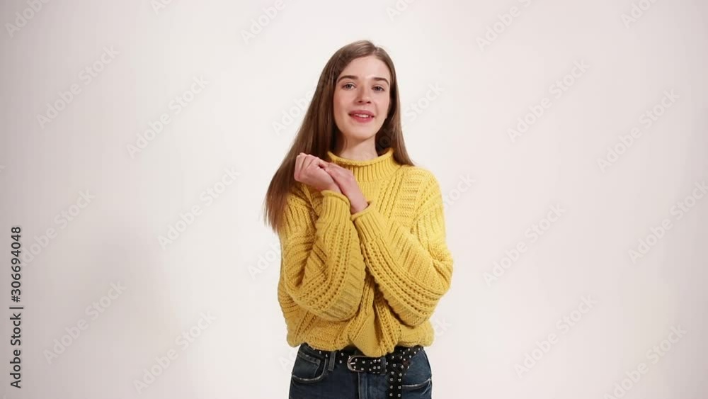 Pleased happy girl wears yellow sweater holds hands together isolated over white background Pleased happy girl wears yellow sweater holds hands together isolated over white background