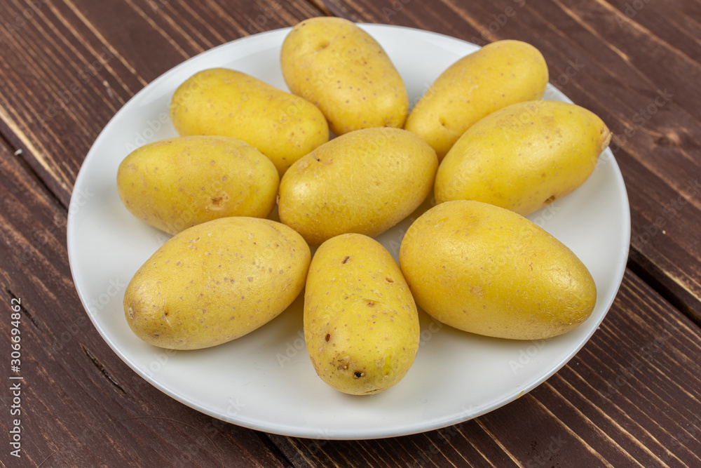 Lot of whole pale yellow potato on white ceramic plate on brown wood Lot of whole pale yellow potato on white ceramic plate on brown wood