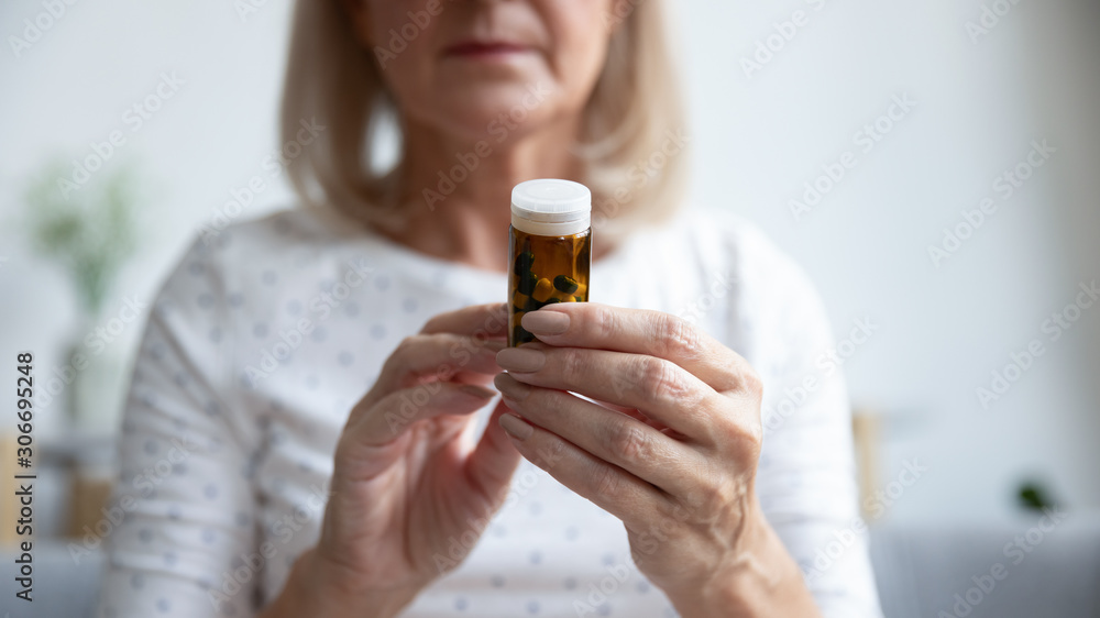 Fototapeta premium Closeup focus on elderly woman hands holding bottle of pills
