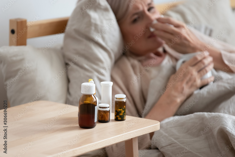 Woman lying in bed focus on nightstand full of medications Woman lying in bed focus on nightstand full of medications
