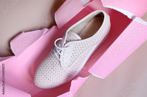 White sneakers on pink paper background with torn hole for copy space. Top view. Minimalism fashion concept.