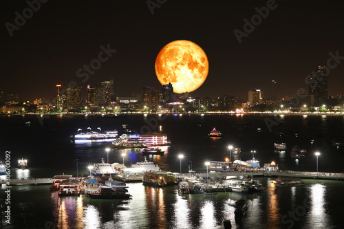 full oak blood moon and night lights of pier and beach and reflection color on water surface of light of city