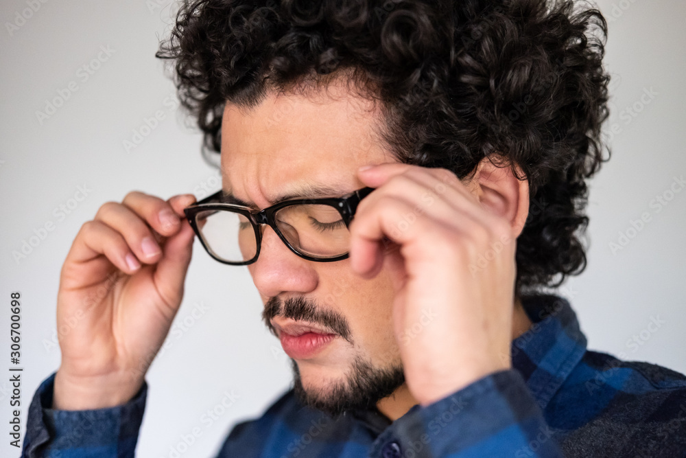 Latin American man with curly hair and glasses, looking upset, worried expression, closed eyes, on a white background  