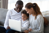 Cheerful mixed race family sitting on sofa, holding laptop.