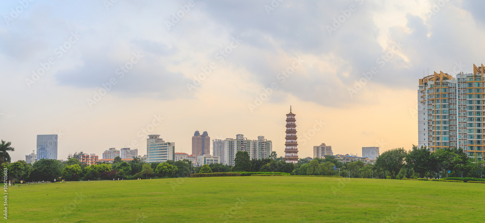 Obraz premium A beautiful panoramic view of tall buildings and Banyan Trees or Liurong temples and a grassy field in the evening against the orange sky in Guangzhou, Guangdong Province, China.