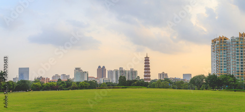 A beautiful panoramic view of tall buildings and Banyan Trees or Liurong temples and a grassy field in the evening against the orange sky in Guangzhou, Guangdong Province, China.