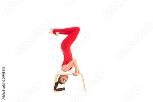 European brunette girl in a red tracksuit wishes gymnastic exercises upside down on a white background