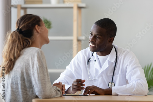 Smiling young woman visiting african american doctor.