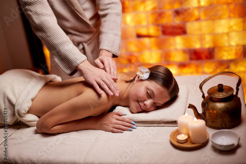 Professional and successful masseur doing massage on shoulders of young lady lying down on desk in spa salon
