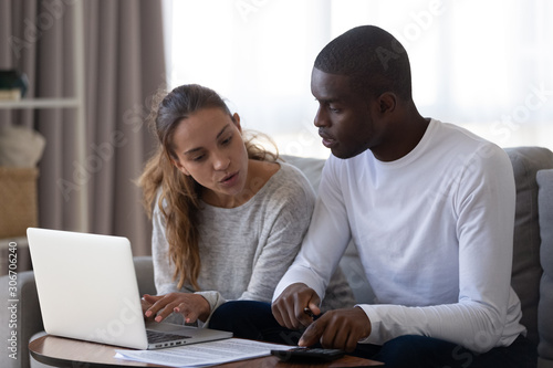 Millennial multiracial married couple calculating monthly family budget.