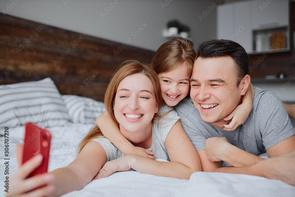 happy caucasian parents lying on bed together with kid girl, having leisure time together at home