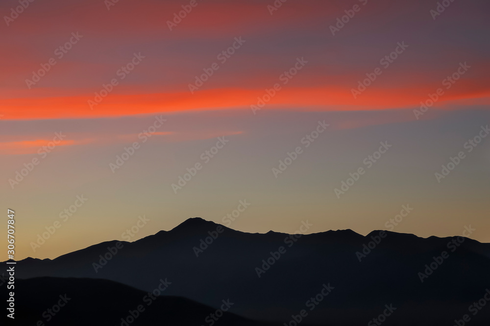 alpine landscape at sunset, vivid red clouds in the pale sky, distant mountain range covered with evening haze, Mongolia