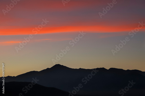 alpine landscape at sunset, vivid red clouds in the pale sky, distant mountain range covered with evening haze, Mongolia