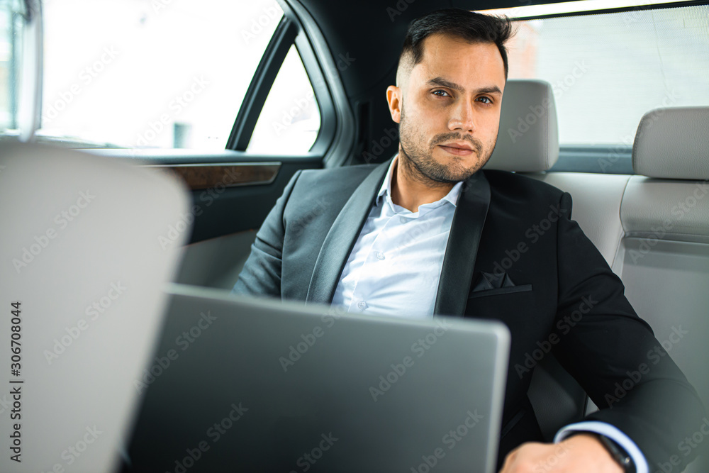 Portrait of caucasian man wearing formal wear sit with laptop in expensive luxurious car, look at camera