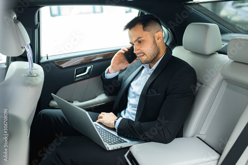 handsome young man sitting in his expensive car of top class, talking on phone and using laptop © alfa27