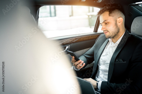 side view on man holding smartphone and looking at screen, sit in executive car wearing formal wear © alfa27