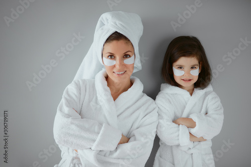 attractive mother with her small daughter wearing bathrobes , with eye patches on face. beauty procedures with child