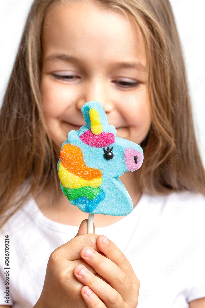 Joyful, happy child holds a unicorn lollipop in his hand on a white background. Close-up trend.