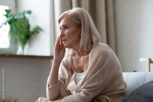 Pensive middle-aged woman seated on couch lost in thoughts