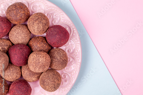 Close Up of Homemade Raw Vegan Cacao Energy Balls on Vintage Plate on Trend Blue and Pink Paper Background. Healthy Chocolate Snacks from Nuts and Dates. Concept of Natural Vegetarian Handmade Dessert