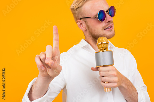cheeky european man in a white shirt speaks into microphone isolated yellow background.