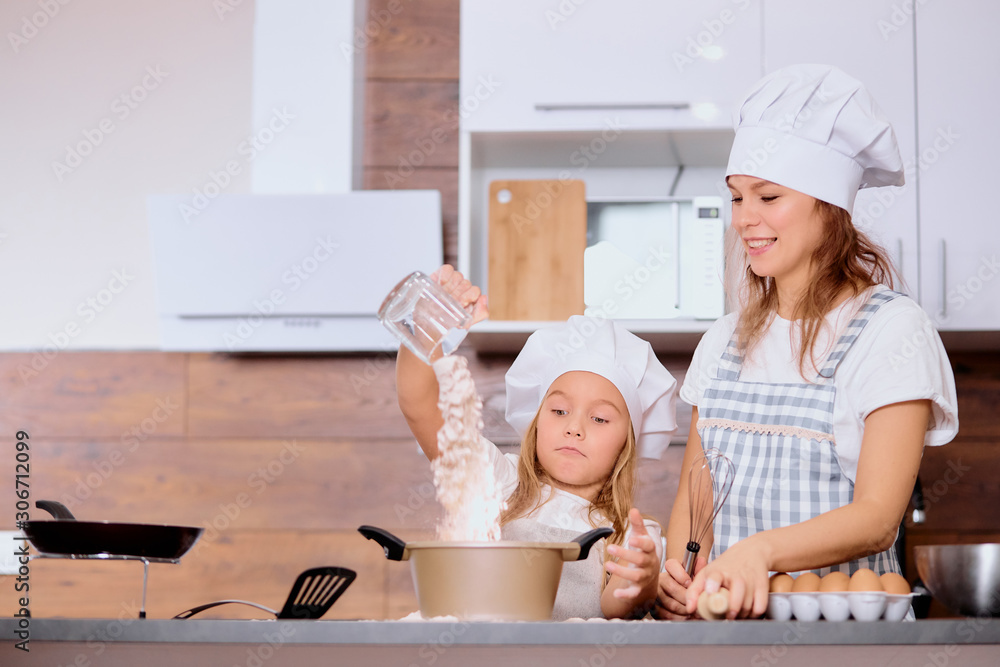 enjoy baking and cooking with mother. litttle girl sprinkling flour from cap before baking cake, using chicken eggs enjoy baking and cooking with mother. litttle girl sprinkling flour from cap before baking cake, using chicken eggs
