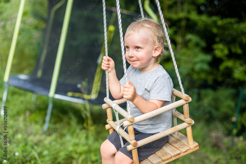 Cute little boy playing on swing in backyard at coutryside