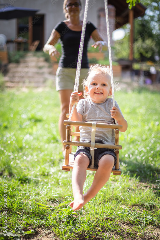 Happy mother pushing laughing son on swing in backyard
