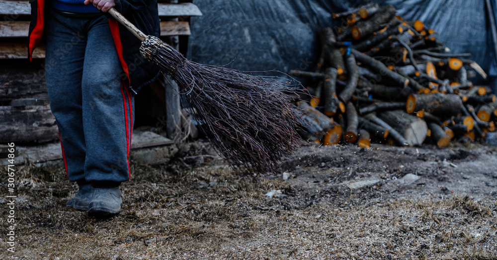 Obraz premium Cleaning in the yard in late fall, a woman with a broom cleans her yard.