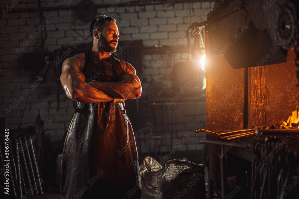 Fototapeta premium serious brutal blacksmith makes metal for future manufacturing isolated in workshop