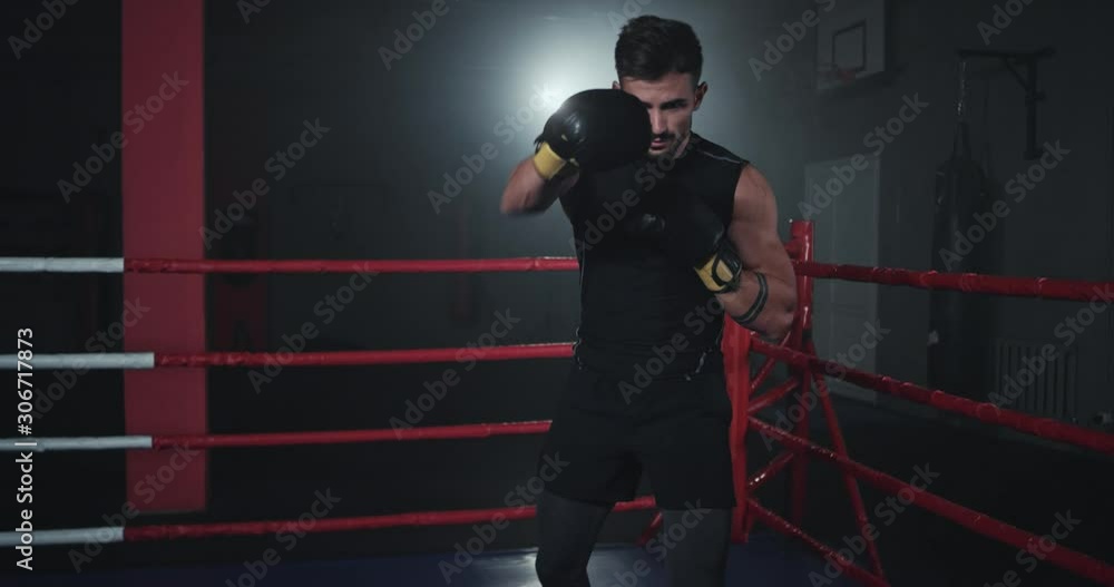 Boxing guy in front of the camera in a dark gym class in the middle of boxing ring Boxing guy in front of the camera in a dark gym class in the middle of boxing ring
