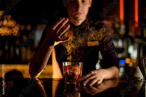 Professional bartender drop an essence to a a glass with cocktail with ice in the smoke