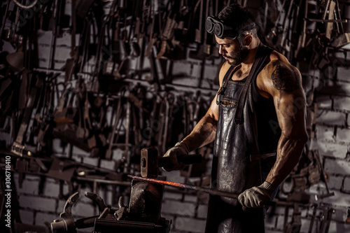 young muscular blacksmith man manually forging the molten metal. Blacksmith hammering hot metal arrow blade, wearing leather apron