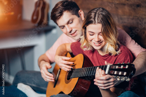 lovely couple, young people playing guitar together at home sitting on bed. caucasian girl and boy wearing casual home clothes
