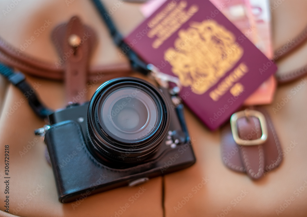 Retro style digital camera and passport on a tan coloured photography bag. Selective focus on the camera lens with intentional out of focus background