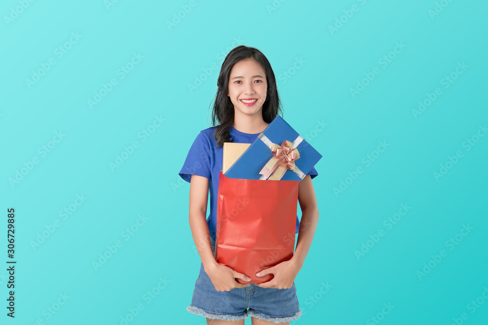 Young smiling Asian woman in t-shirt holding blue gift on light background. Young smiling Asian woman in t-shirt holding blue gift on light background.