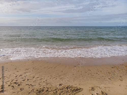 A view of a sandy beach with small crashing wave under a beautiful cloudy blue sky photo