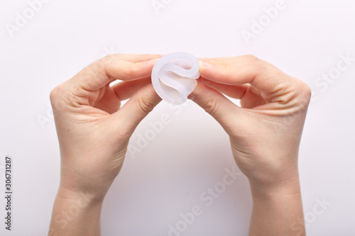 Horizontal shot of woman hands holding white menstrual cup, top view, twisting it, sticking to rules of usage, showing its possibilities, type of feminine hygiene product, menstrual cycle concept. photo