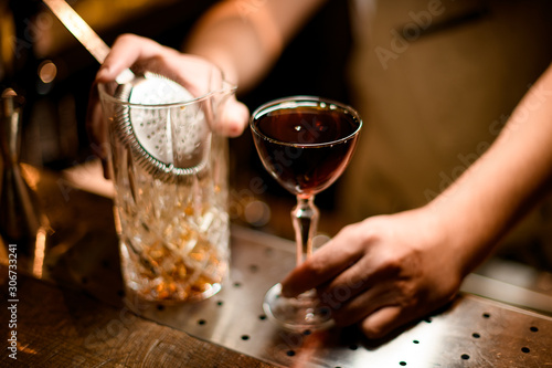Close-up of strainer in glass and cocktail in bartender's hand
