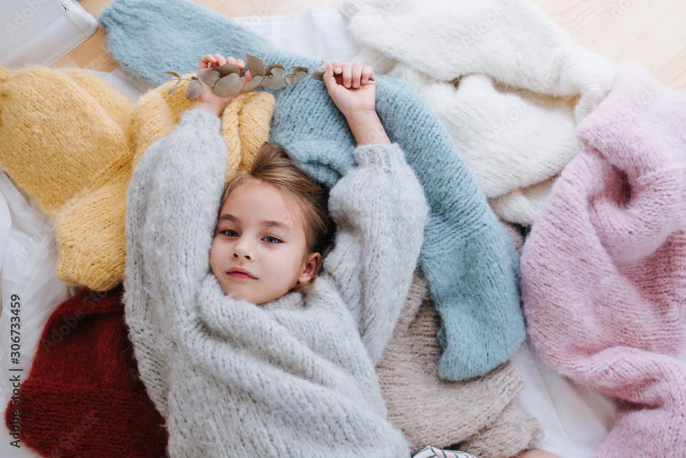 Sleepy little girl is lying on a pile of soft multi-colored sweaters on the floor. Sleepy little girl is lying on a pile of soft multi-colored sweaters on the floor.