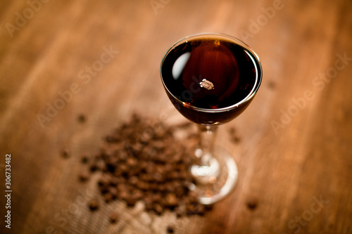 Dark alcohol cocktail with coffee beans stands on wooden table