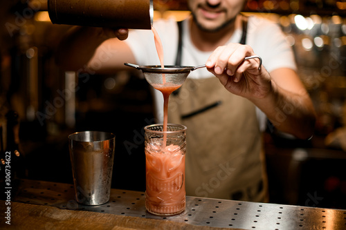 Bartender flows drink through sieve to glass