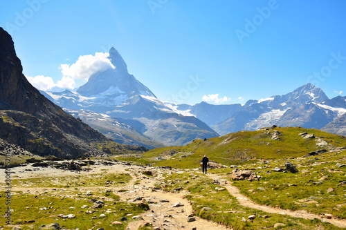 Wide view of the Matterhorn (with cloud climbing its side) along the path towards the Riffelsee Lake with a hiker on trail, Zermatt, Switzerland photo