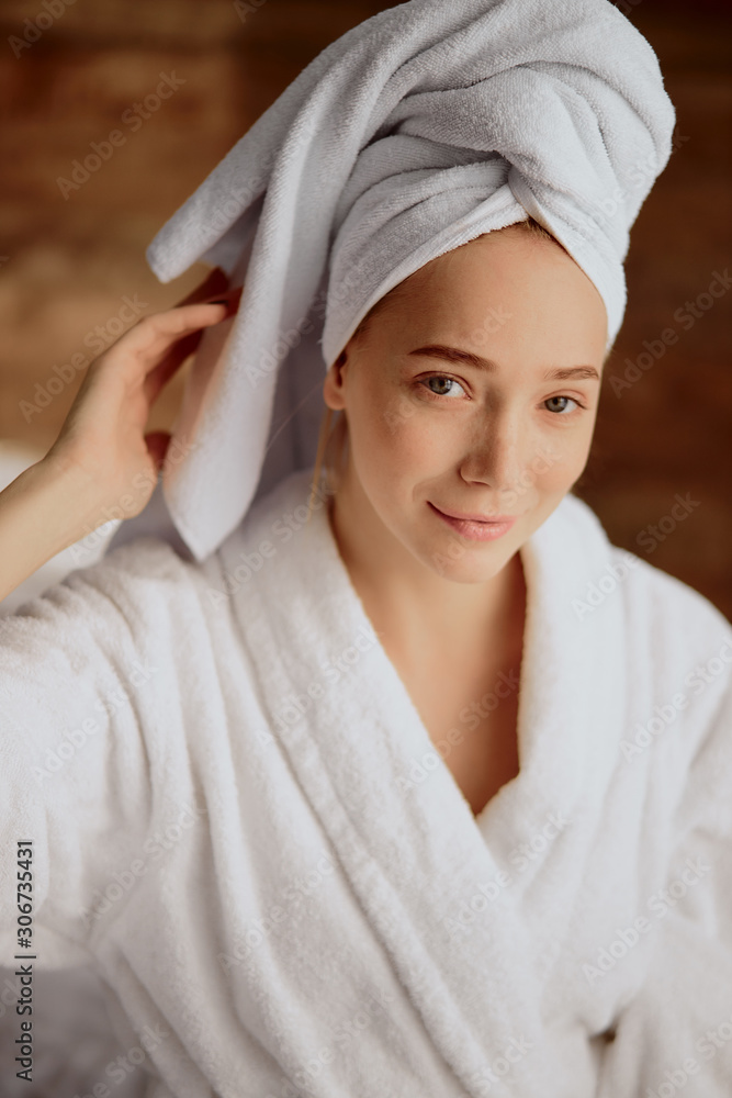 Beautiful young woman after bath with towel wrapped on head, looking straight at camera with charming smile, raising hand up, portrait, natural beauty concept Beautiful young woman after bath with towel wrapped on head, looking straight at camera with charming smile, raising hand up, portrait, natural beauty concept