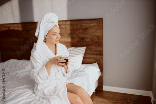 Optimistic romantic girl starting day with cup of fresh tasty black coffee, holding in hands, looking at window, dreaming with positive emotions, expressing pleasant feelings, indoor shot