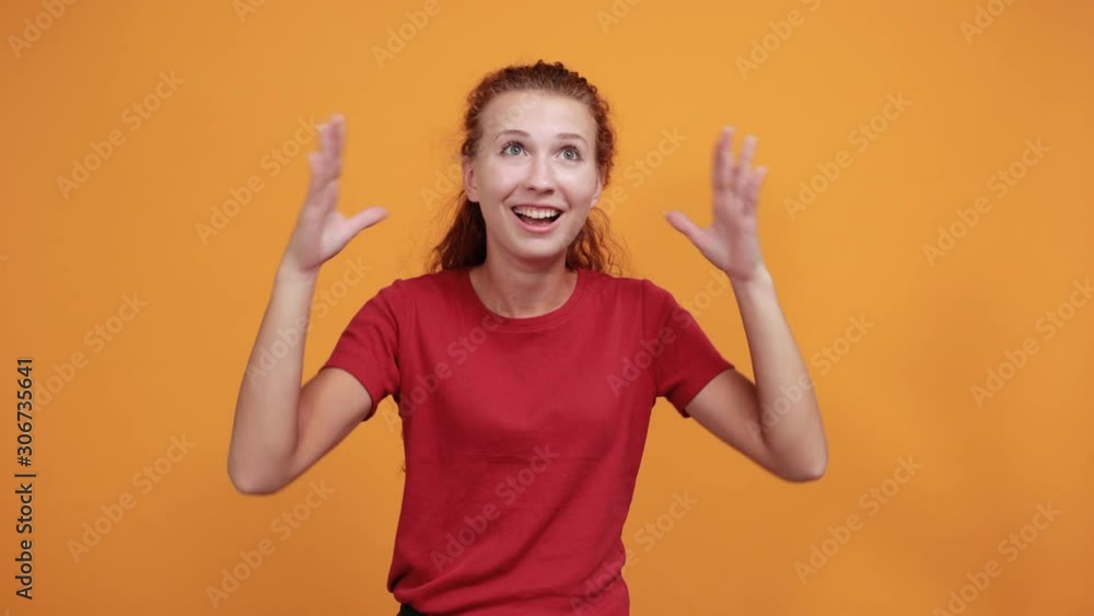 Pretty young woman in red shirt keeping hands spreads isolated on orange background in studio. People sincere emotions, health concept. Pretty young woman in red shirt keeping hands spreads isolated on orange background in studio. People sincere emotions, health concept.