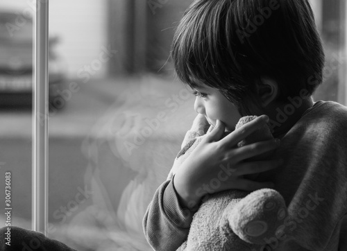 Emotional portrait of upset little boy sitting next to window, Kid sad face,Dramatic photo of Unhappy child looking down, Lonely boy sitting with his teddy bear, Spoiled children concept