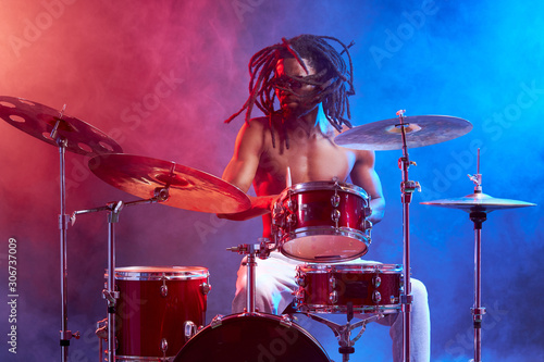 vigorous male with naked skin playing on drums isolated over neon smoky background, wearing eyeglasses